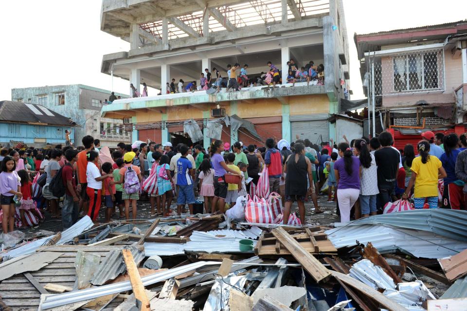 Residents watch others throw items out from a warehouse after super typhoon Haiyan hit Guiuan