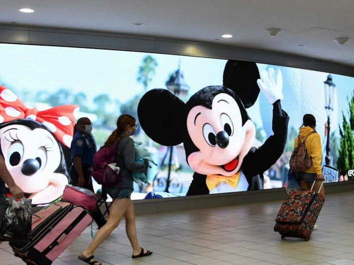 Crowds walk past a sign advertising Walt Disney World at Orlando International Airport.