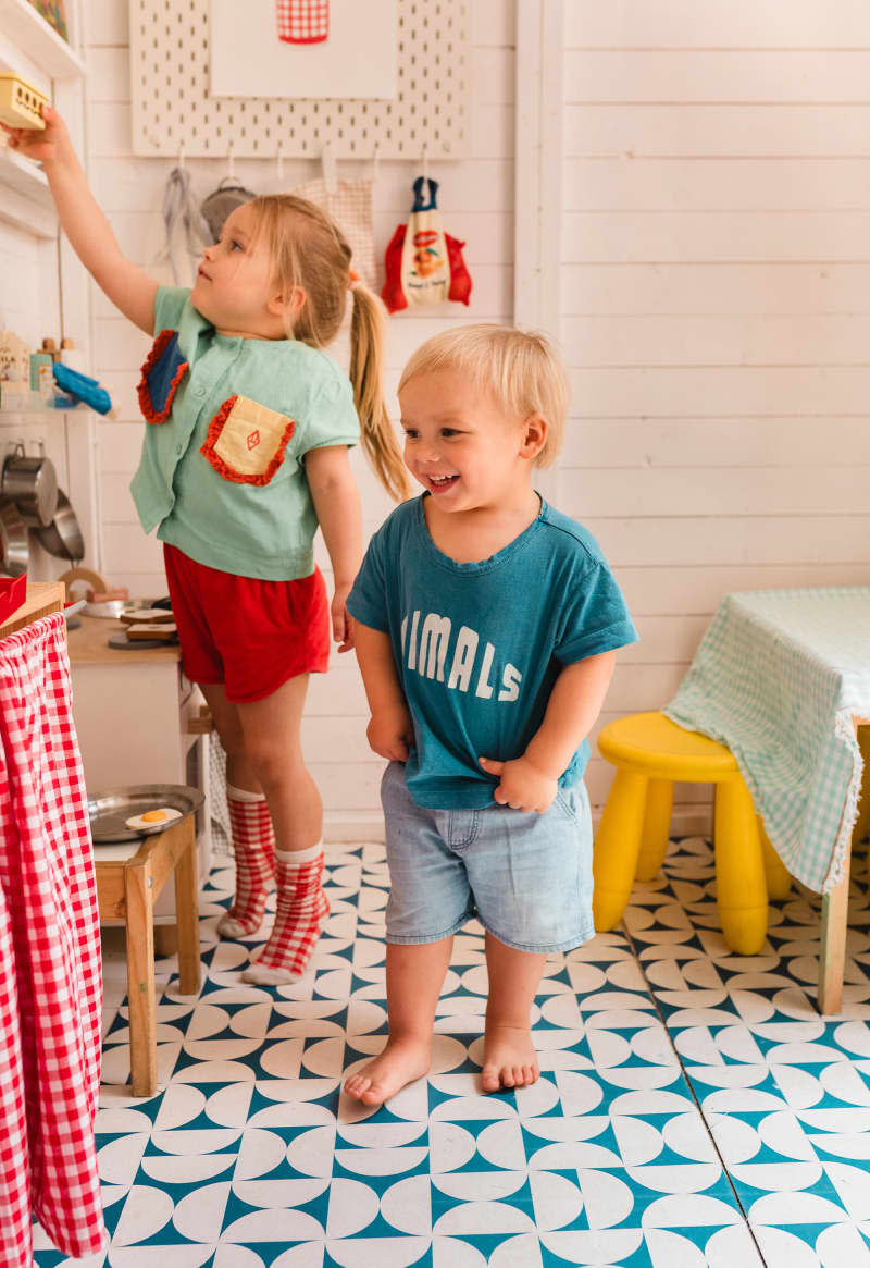 2 kids playing in play kitchen with blue and white patterned floor