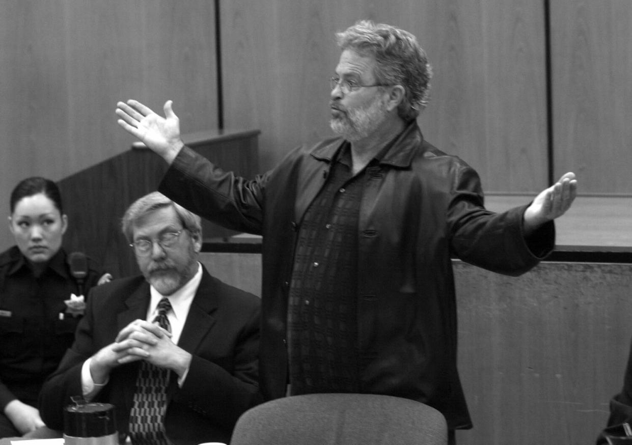 A man holds his arms out to his sides while he speaks in court.