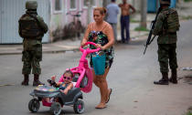 <p>Eine Frau schiebt ihr Kind in der Vila-Kennedy-Favela in Rio de Janeiro in einem pinken Auto-Buggy über die Straße, während hinter ihr zwei Soldaten mit Maschinengewehren stehen. Das brasilianische Militär soll in dem Slum gegen organisierte Kriminalität vorgehen. (Bild: MAURO PIMENTEL/AFP/Getty Images) </p>