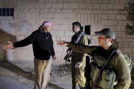 A Palestinian man speaks with Israeli soldiers as they search for a missing Israeli near the West Bank city of Hebron April 2, 2015. REUTERS/Ammar Awad