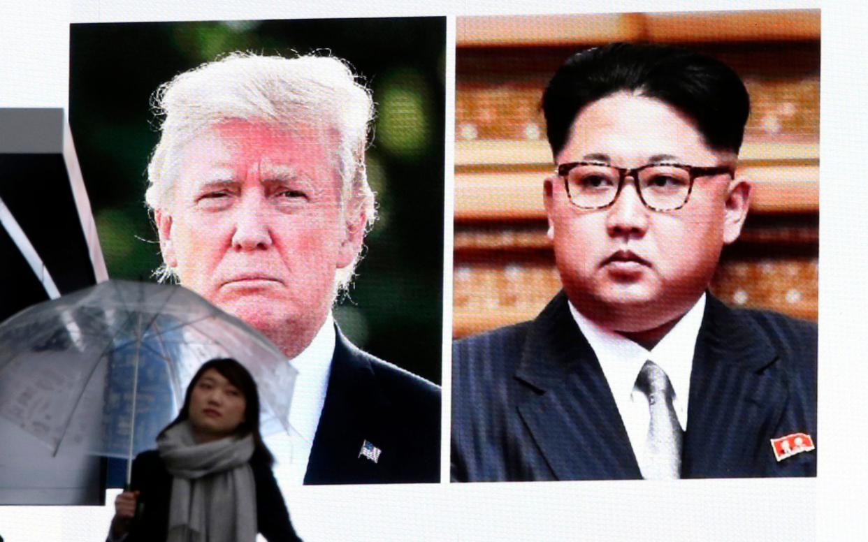 A woman walks by a huge screen showing U.S. President Donald Trump, left, and North Korea's leader Kim Jong Un, in Tokyo - AP