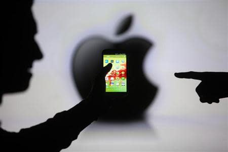 Men are silhouetted against a video screen with an Apple Inc logo as they pose with a Samsung Galaxy S3 smartphone in this photo illustration taken in the central Bosnian town of Zenica, May 17, 2013. REUTERS/Dado Ruvic