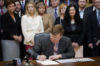 Mississippi Gov. Tate Reeves signs the first state bill in the U.S. this year to ban transgender athletes from competing on female sports teams, as supporting lawmakers gather behind him, Thursday, March 11, 2021, at the Capitol in Jackson, Miss. (AP Photo/Rogelio V. Solis)