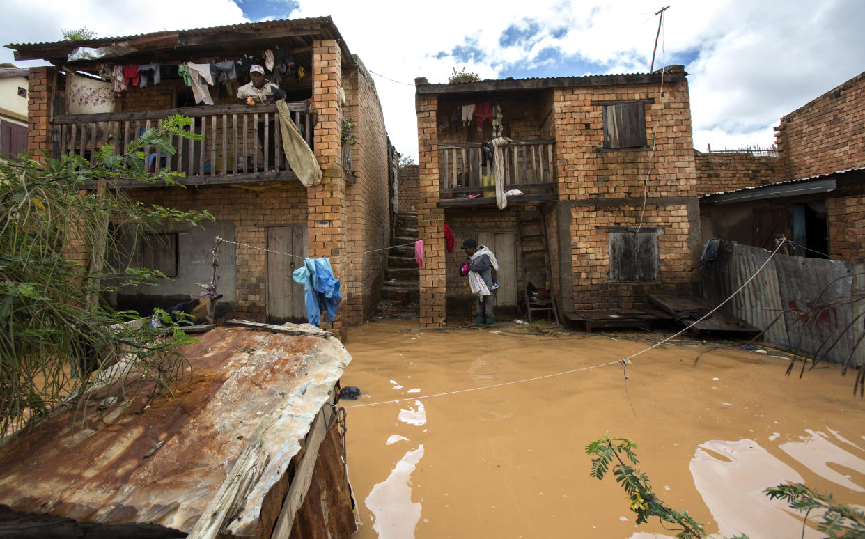 A man holding a child on his back stands on a doorstep flooded with rain water in Antananarivo, Madagascar, Saturday, Jan. 28, 2023. A tropical storm Cheneso made landfall across north-eastern Madagascar on January 19, brought strong winds to coastal regions, while heavy rain brought significant flooding to northern parts of the country. (AP Photo/Alexander Joe)