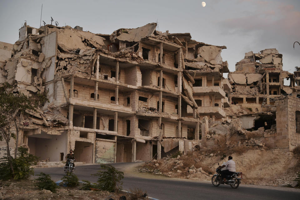 FILE - In this Sept. 20, 2018, file photo, motor cycles ride past buildings destroyed during the fighting in the northern town of Ariha in Idlib province, Syria. As world leaders talk peace at the U.N. this week, the Syrian region of Idlib clings to fragile hope that diplomacy will help avert a blowout battle over the country’s last rebel stronghold. (Ugur Can/DHA via AP, File)