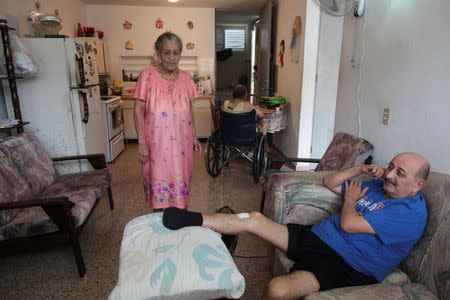 Juanita Gomez Cruz (L), stands in her home next to her husband Pedro (R), who lost part of his leg due to diabetes, as their son Dafner sits in a wheelchair at a table, in San Juan, Puerto Rico, November 15, 2016. REUTERS/Alvin Baez