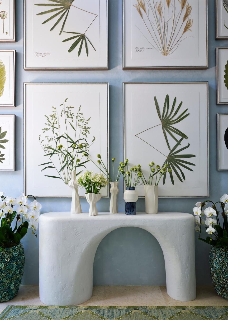 Framed botanicals hang above a freeform console table in the stair hall designed by Charlie Collins of MELROSE for the Kips Bay Decorator Show House Palm Beach.