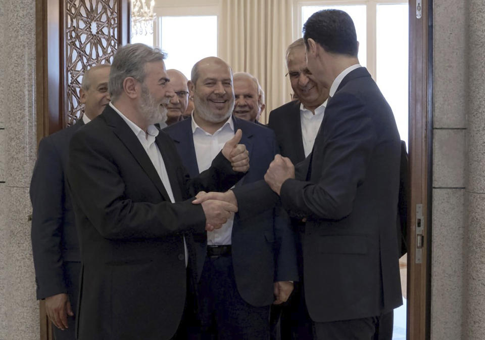 In this photo released by the Syrian official news agency SANA, Syrian President Bashar Assad, right, shakes hands with Ziad Nakhaleh, leader of the Palestinian Islamic Jihad group, as Khalil al-Hayeh, a senior figure in Hamas' political branch, center, and others wait to greet the president, in Damascus, Syria, Wednesday, Oct. 19, 2022. Al-Hayeh was one of two senior officials from the Palestinian militant Hamas group who visited Syria's capital on Wednesday for the first time since they were forced to leave the war-torn country a decade ago over backing armed opposition fighters. (SANA via AP)