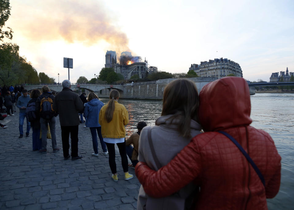 People watch as flames and smoke rise from Notre Dame cathedral as it burns in Paris, Monday, April 15, 2019. Massive plumes of yellow brown smoke is filling the air above Notre Dame Cathedral and ash is falling on tourists and others around the island that marks the center of Paris. (AP Photo/Thibault Camus)