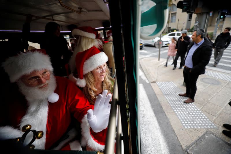 People dressed in Santa Claus outfits wave from inside a bus as they make their way to visit Jerusalem's Old City as a group of Santa Clauses from around the world, in Jerusalem