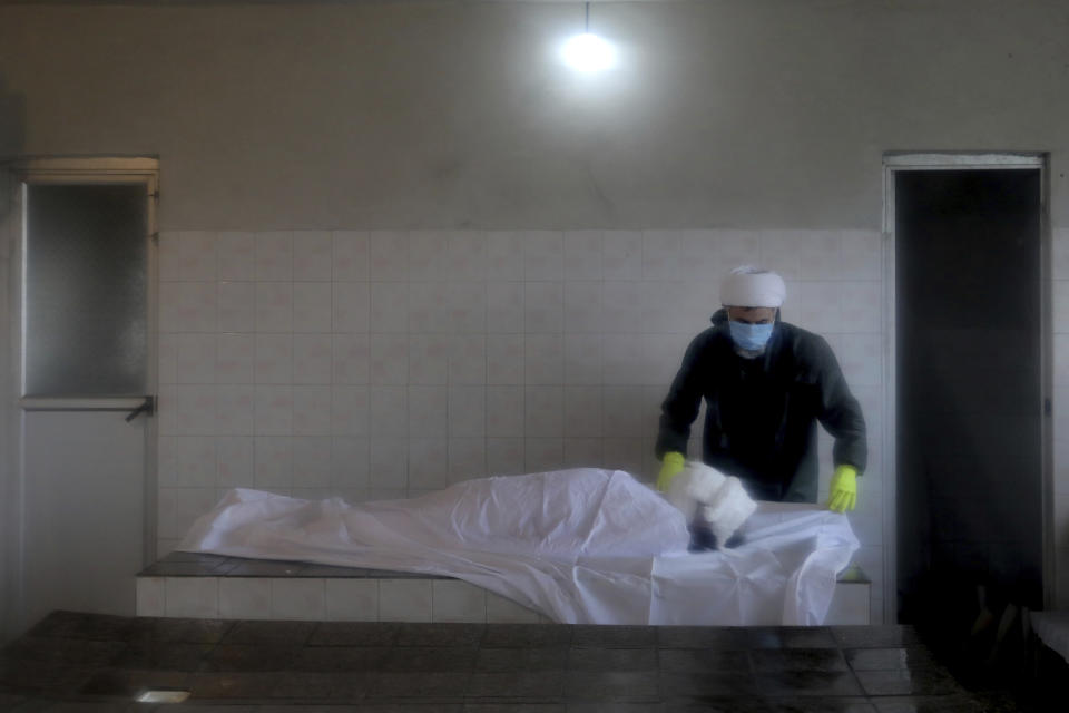 A cleric wearing protective clothing prepares the body of a man who died from COVID-19 for a funeral at a cemetery in the outskirts of the city of Ghaemshahr, in northern Iran, Saturday, Dec. 19, 2020. (AP Photo/Ebrahim Noroozi)