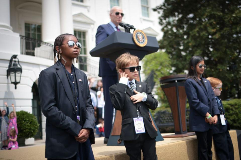 Biden speaks while children dressed as Secret Service agents "guard" the stage on Take Your Child To Work Day