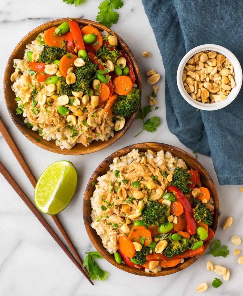 peanut chicken with veggies in two wood bowls with chopsticks and lime wedges