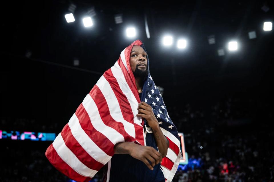 Kevin Durant wraps himself in the American flag Saturday after Team USA defeated France in the gold medal men's basketball game of the 2024 Paris Olympics. The former All-American at Texas became the first U.S. men's player to win four gold medals, and he also became the all-time leading Olympic scorer for the U.S. men's or women's teams.