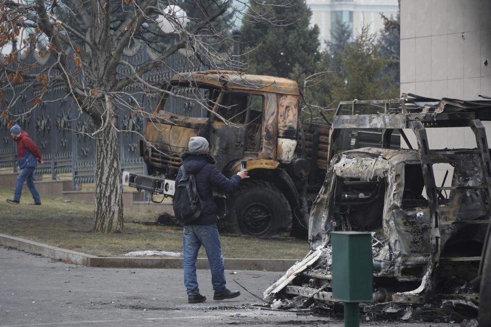 A man photographs a bus, which was burned during clashes in Almaty, Kazakhstan, Tuesday, Jan. 11, 2022. Life in Almaty, which was affected with the violence the most during protests, started returning to normal this week, with public transport resuming operation and malls reopening. (Vladimir Tretyakov/NUR.KZ via AP)