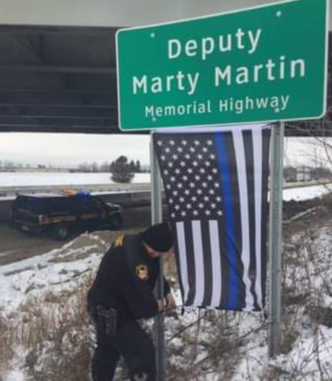 A member of the Franklin County Sheriff's office installs a new "Thing Blue Line" flag on the memorial highway sign for Deputy Marty Martin.