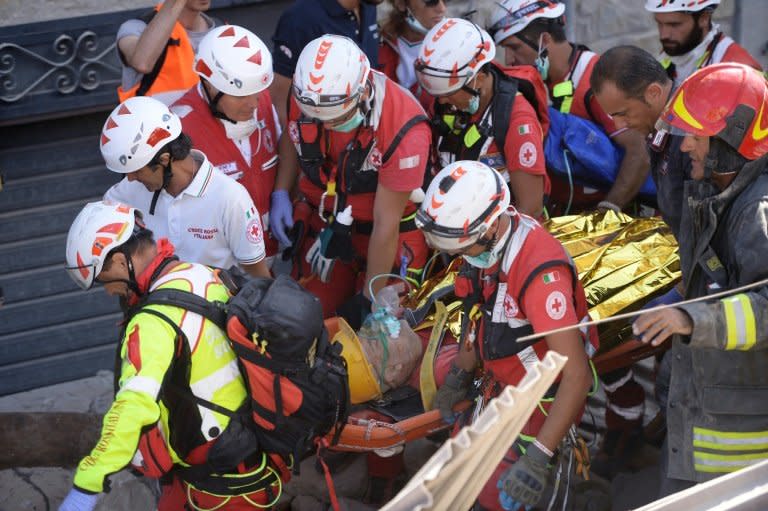 Rescue and emergency services personnel carry a survivor on a stretcher during search and rescue operations in Amatrice