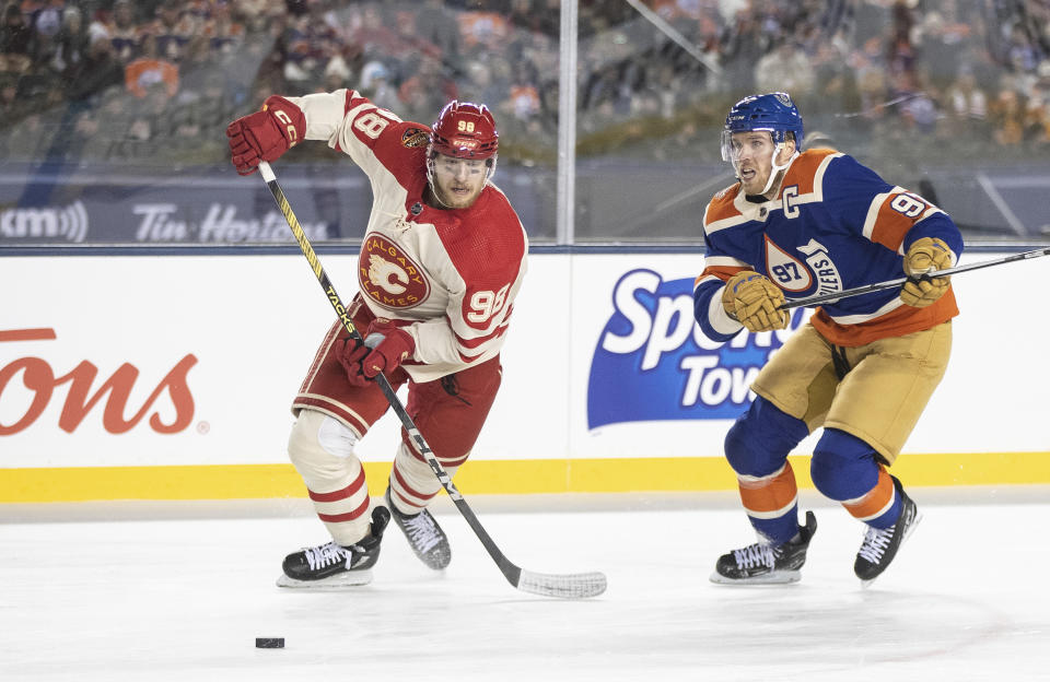 Calgary Flames' Ilya Solovyov (98) and Edmonton Oilers' Connor McDavid (97) chase the puck during third-period NHL Heritage Classic outdoor hockey game action in Edmonton, Alberta, Sunday, Oct. 29, 2023. (Jason Franson/The Canadian Press via AP)