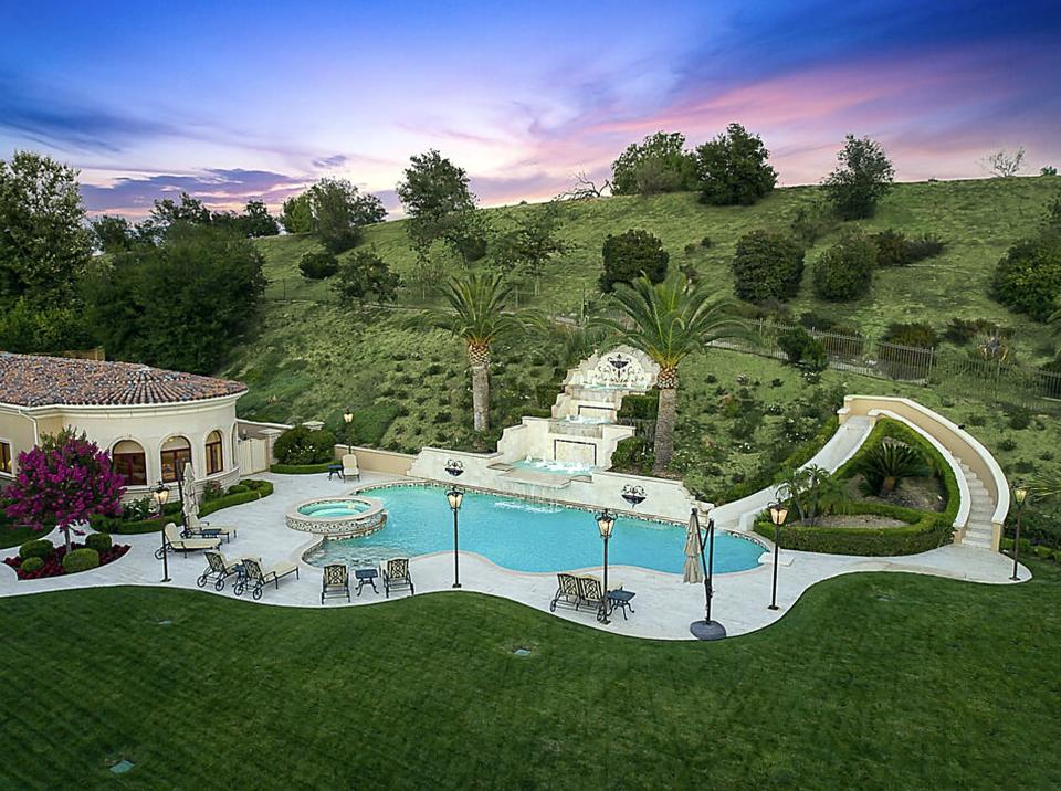 An oddly shaped pool that has a slide built into one side and a hot tub on the opposite side