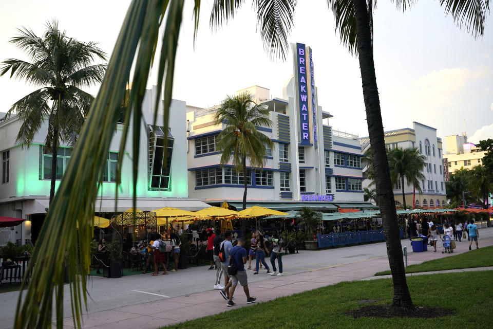 People walk along Ocean Drive, Friday, Sept. 24, 2021, in Miami Beach, Fla. Cooped-up tourists eager for a taste of Florida's sandy beaches, swaying palm trees and warmer climates are visiting the Sunshine State in droves, topping pre-pandemic levels in recent months. (AP Photo/Lynne Sladky)