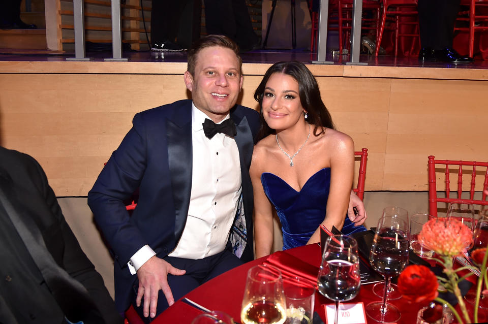 Two people seated at a table, one in a tuxedo and the other in a strapless blue gown