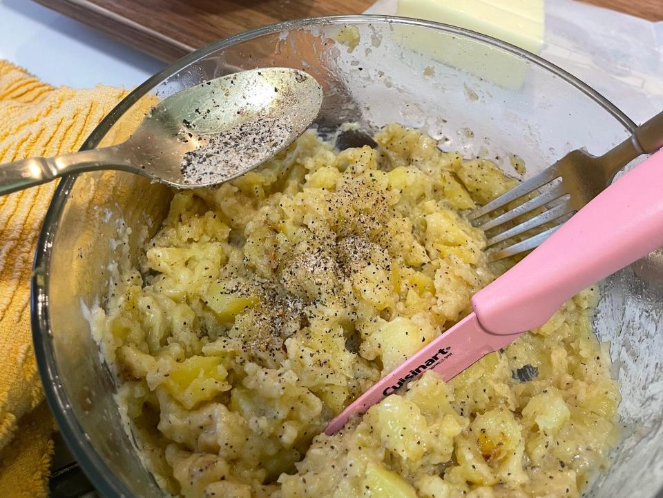 bowl of semi-mashed potatoes with seasoning, knife, and fork in it