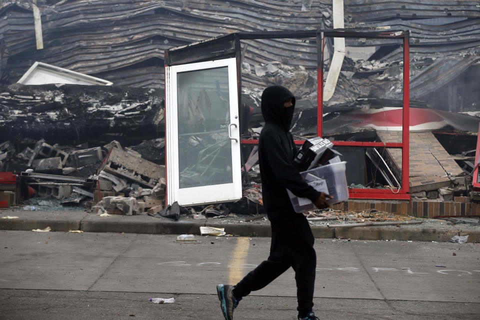 Un hombre carga unos objetos mientras camina frente a una tienda de Auto Zone quemada, el jueves 28 de mayo de 2020, en Minneapolis, Minnesota. (AP Foto/Jim Mone)