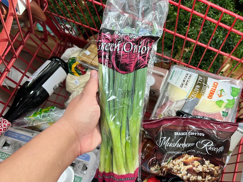 hand holding bunch of green onions above a shopping cart at trader joe's