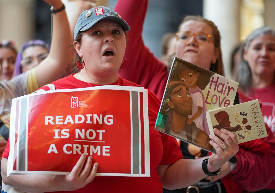 Courtney Atak, an eighth grade social studies teacher at Brown County Middle School, holds up books while rallying at the Indiana Statehouse on Thursday, April 13, 2023, in Indianapolis. Teachers called for more public school funding and spoke in opposition to a bill that would remove many discussion topics from the collective bargaining process, as well as "culture war and book banning bills."