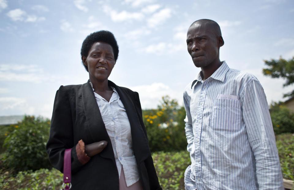 In this photo taken Wednesday, March 26, 2014, Emmanuel Ndayisaba, right, who during the 1994 Rwandan genocide cut off with a machete the hand of Alice Mukarurinda, left, in the swamp where she was hiding and killed her baby girl, but who are now friends, pose for a photograph outside Alice's house in Nyamata, Rwanda. (AP Photo/Ben Curtis)