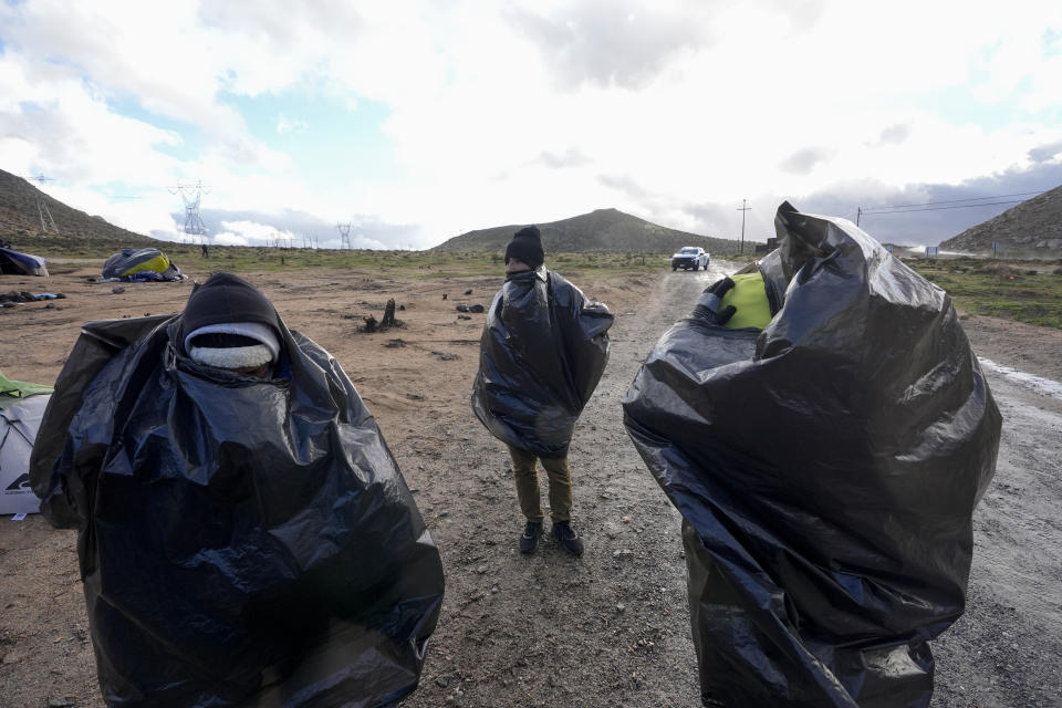 Asylum-seeking migrants wrap themselves in plastic bags to ward off the wind and rain as they wait to be processed in a makeshift, mountainous campsite after crossing the border with Mexico, Friday, Feb. 2, 2024, near Jacumba Hot Springs, Calif. (AP Photo/Gregory Bull)