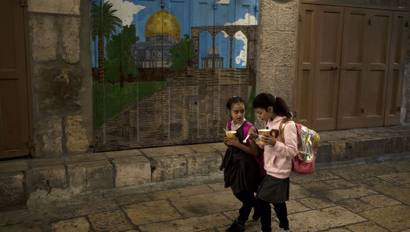 Palestinian girls eat noodles as they walk home from school through a row of storefronts closed for a general strike calling for a cease-fire in Gaza, in the Old City of Jerusalem on Dec. 11, 2023.