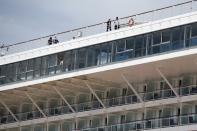 Crew members wearing face masks walk on the deck of a cruise ship that has been docked for almost two months due to the coronavirus outbreak at the port of Piraeus, near Athens, Wednesday, May 20, 2020. Greece's government says revenue from its vital tourism industry has been hammered as a result of the COVID-19 pandemic and lockdown measures, adding that detailed guidelines on how the season will operate will be announced Wednesday. (AP Photo/Thanassis Stavrakis)