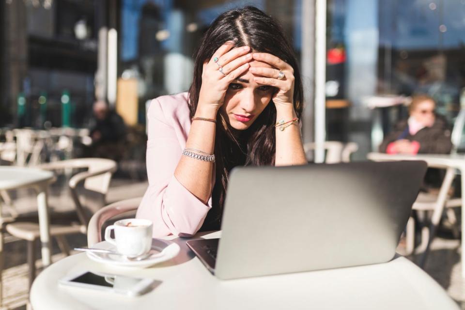 A frustrated woman holds her head as she looks at a laptop