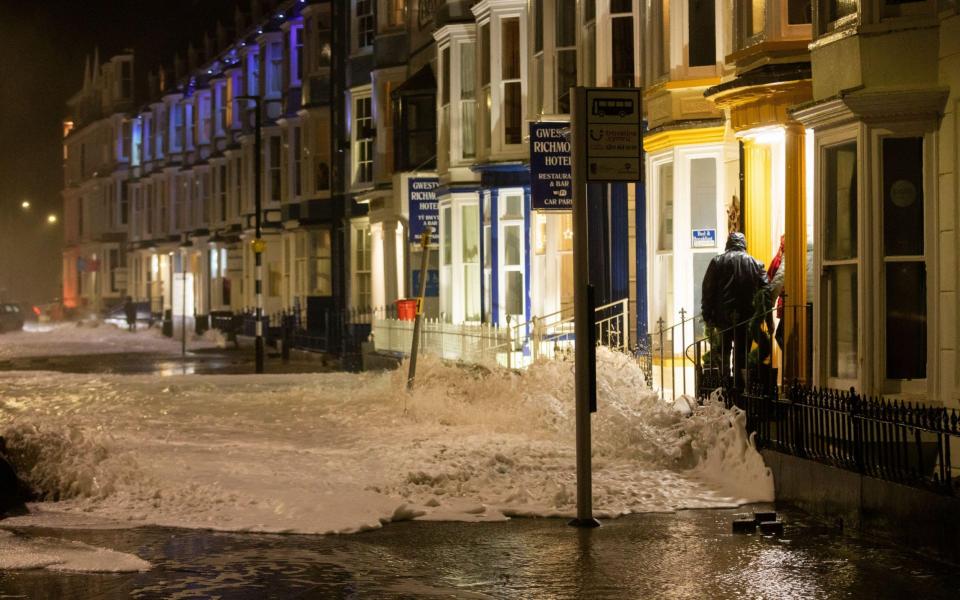 Sandbags are laid at the entrance of a seafront property as water floods the road along Aberystwyth promenade, Wales - Ian Jones / Alamy Live News