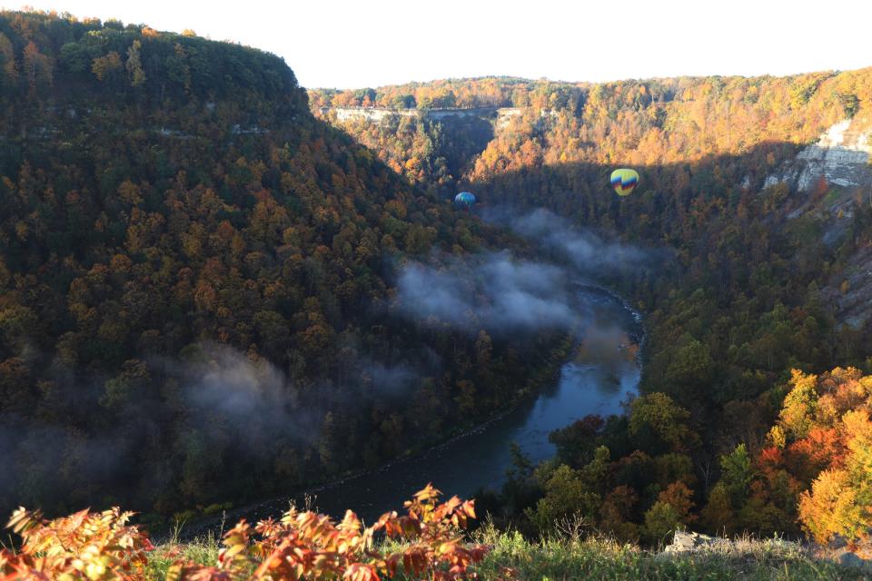 Two hot air balloons winds along the Genesee River gorge at Letchworth State Park before rising up and out.