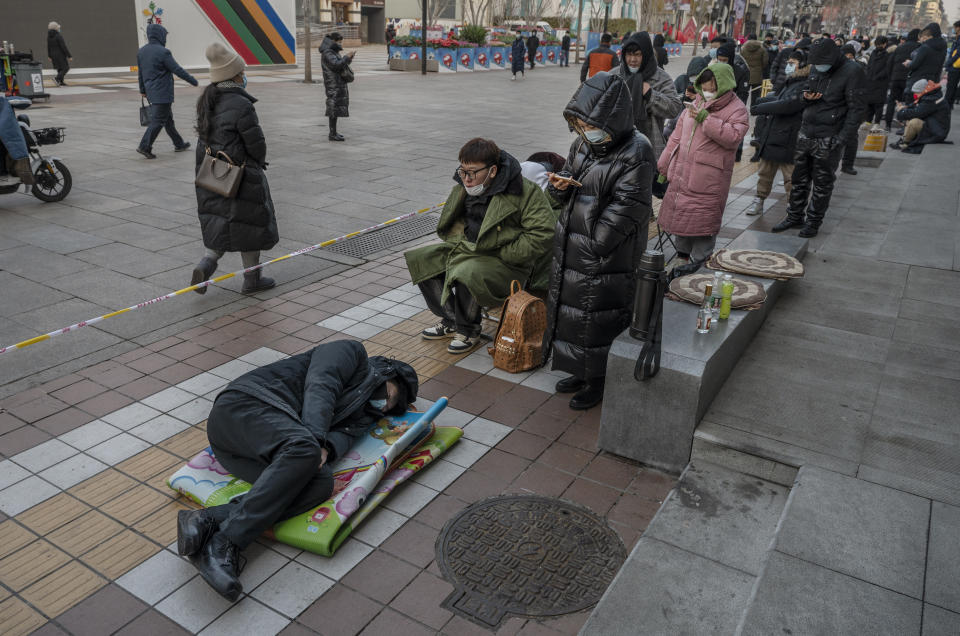 BEIJING, CHINA - FEBRUARY 10: A man rests on the sidewalk as he and others line up outside the official Beijing 2022 Winter Olympics flagship souvenir store early on February 10, 2022 in Beijing, China. Crowds of people have been lining up at authorized Beijing 2022 Winter Olympic stores trying to purchase Bing Dwen Dwen paraphernalia, the panda mascot of the Games. Items featuring the character have become a hot seller that Beijing 2022 merchandise stores cannot keep them in stock. Officials say the factories authorized to produce the souvenirs have been urged to increase production to help boost supplies. The sudden popularity of Bing Dwen Dwen, along with the Paralympic Games mascot Shuey Rhon Rhon, comes as most Chinese fans are unable to attend Olympics events in the host city because of China's zero-COVID protocols. (Photo by Kevin Frayer/Getty Images)