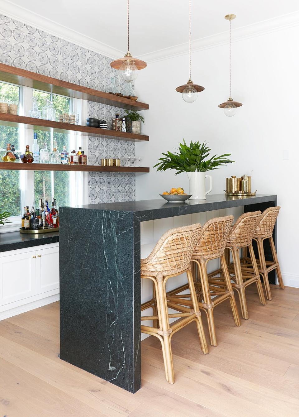 Home bar with waterfall countertop and open wood shelving with woven counter stools