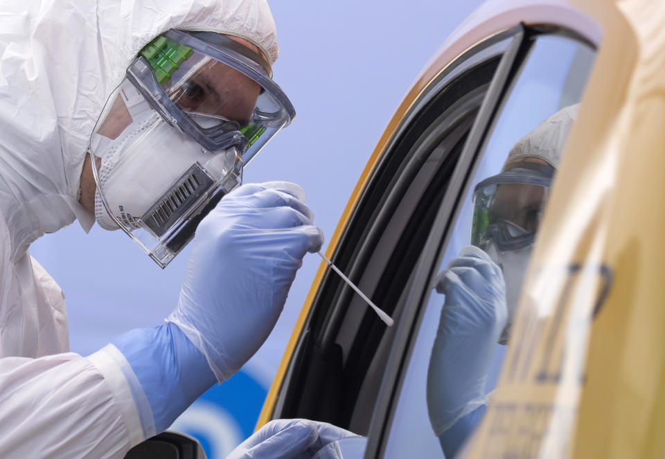 FILE - In this April 15, 2020, file photo, helper of the German Red Cross DRK in protective suit, left, takes a smear from a patient in his car during the official opening of a drive-thru COVID-19 testing center at the fair ground in Dresden, eastern Germany. As the restrictions to avoid the spreading of the coronavirus are eased, Chancellor Angela Merkel has pointed to South Korea as an example of how Germany will have to improve measures to “get ahead” of the pandemic with more testing and tracking of cases so that the rate of infections can be slowed. (AP Photo/Jens Meyer, File)