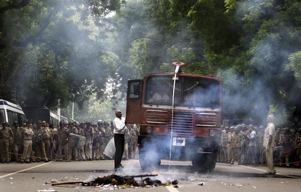 An Indian policeman tries to douse flames from an effigy representing the ruling United Progressive Alliance (UPA) government set afire by the main opposition Bharatiya Janata Party (BJP) activists during a protest in New Delhi, India, Saturday, Sept. 15, 2012. India's beleaguered government faced angry protests from its political allies as well as the opposition after it raised the price of diesel fuel in a bid to curb a ballooning national deficit and also announced a reduction in cooking gas subsidies. (AP Photo/Altaf Qadri)