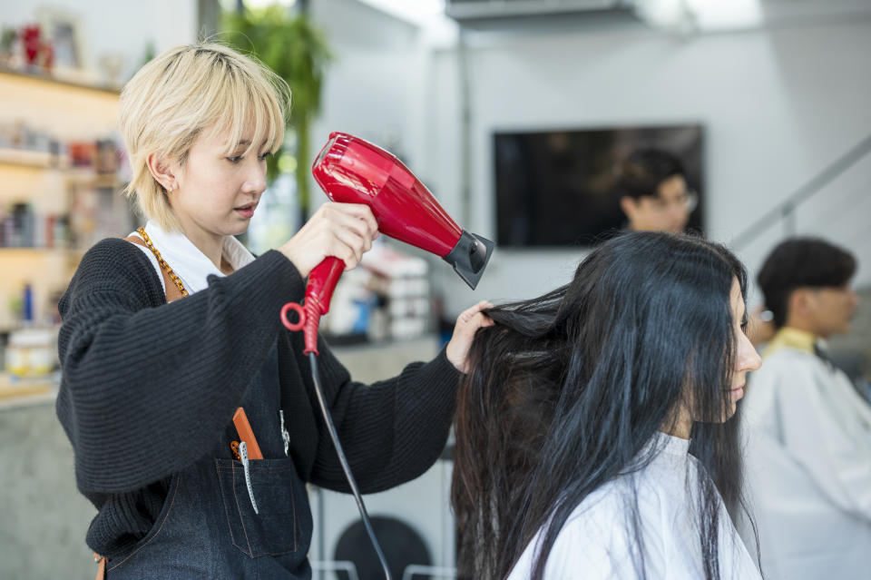 Asian hairdresser is using a dryer for customer after washing hair in hair salon. Beauty salon business.
