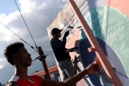 Artist Fabian Solymar paints a mural with a member of the community in Petare slum, in Caracas