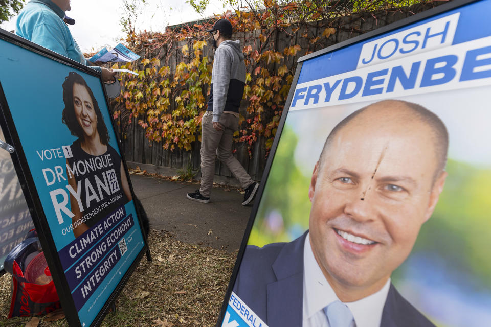 Signs displaying photos of politicians Monique Ryan and Josh Frydenberg and a person handing out how to vote cards