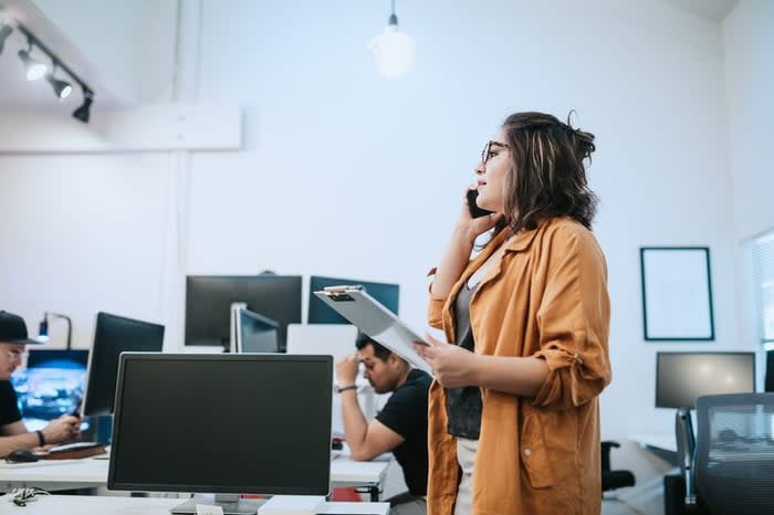 Woman in office holding clipboard and talking on phone.