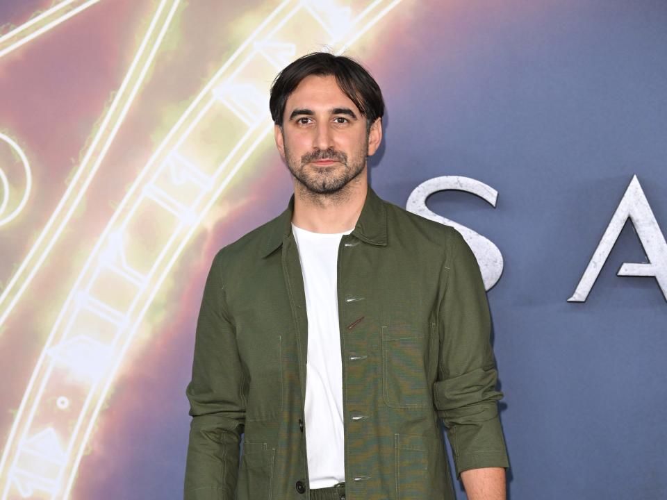 ferdinand kingsley on the sandman red carpet. he's wearing a casual-appearaning forest green suit set, with an unbuttoned jacket over a white shirt. he has slight facial hair and short hair