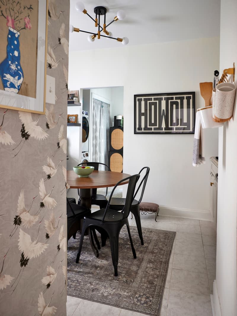 Graphic text art on wall in neutral kitchen with drop-leaf pedestal table and metal chairs.