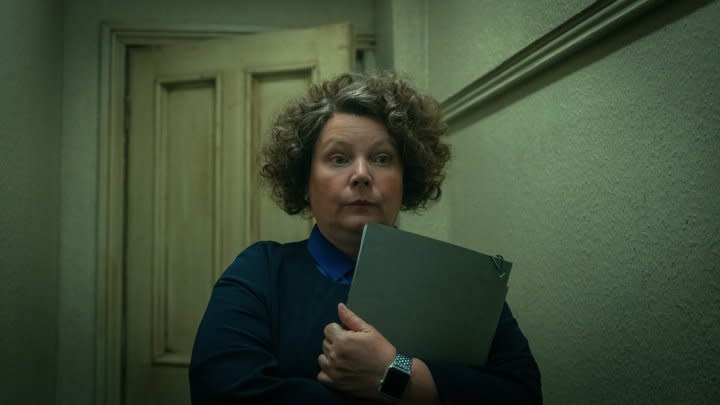 A woman holds a notebook in a hallway.