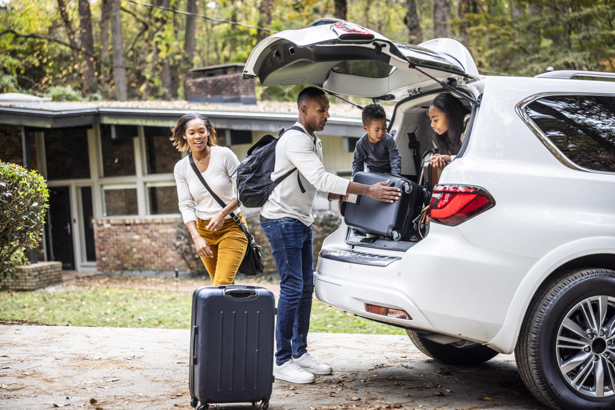 A man, a woman and two children load suitcases into the back of a car.